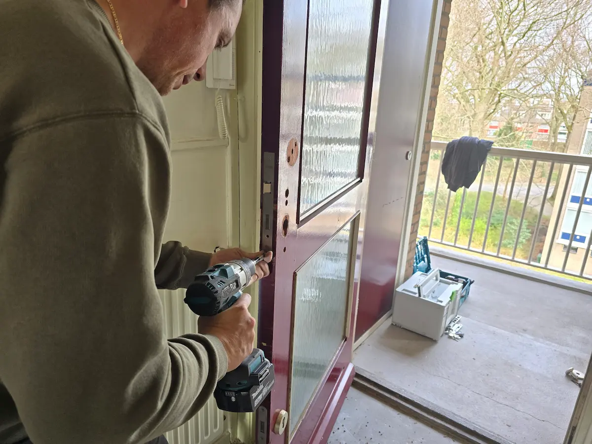 Een slotenmaker aan het werk met een boormachine bij de deuropening van een woning in Bunnik