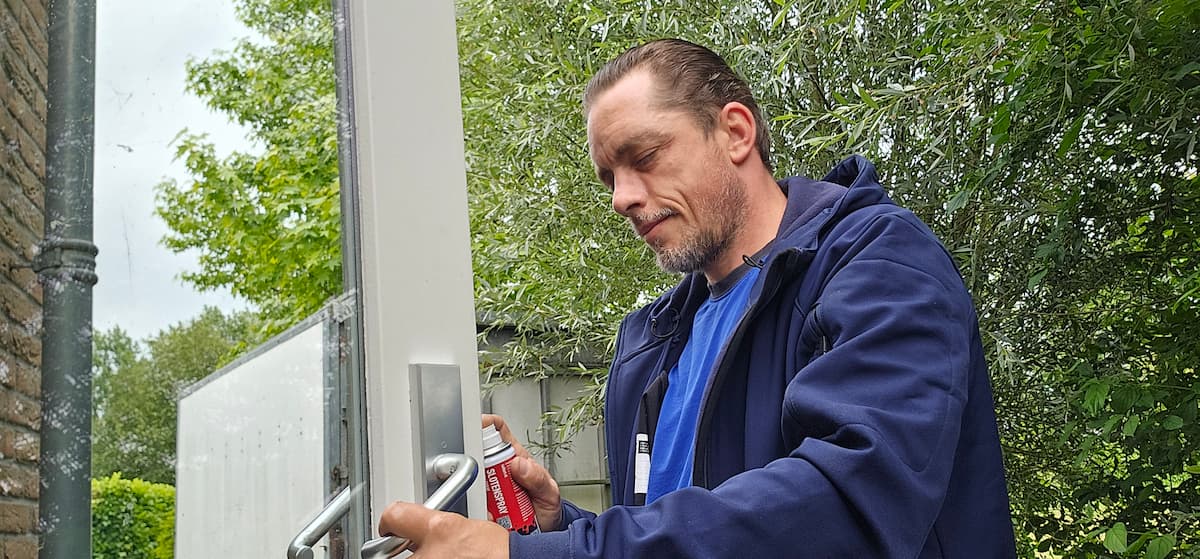 Ervaren slotenmaker in Vianen smeert een deurslot met slotenspray voor optimale werking.