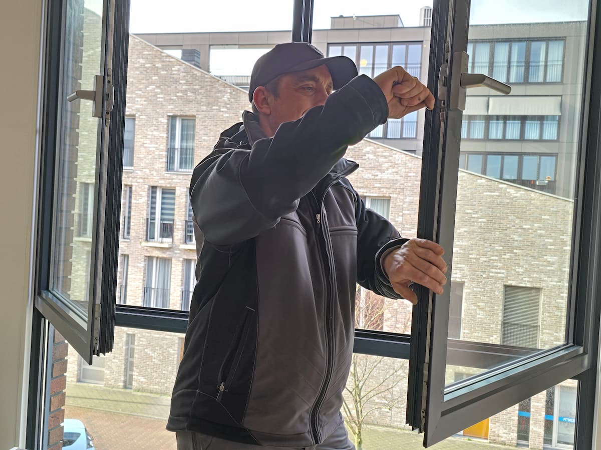 Een slotenmaker van Slotenmaker Bilthoven voert onderhoud uit aan het hang- en sluitwerk van een openstaand kantelraam.