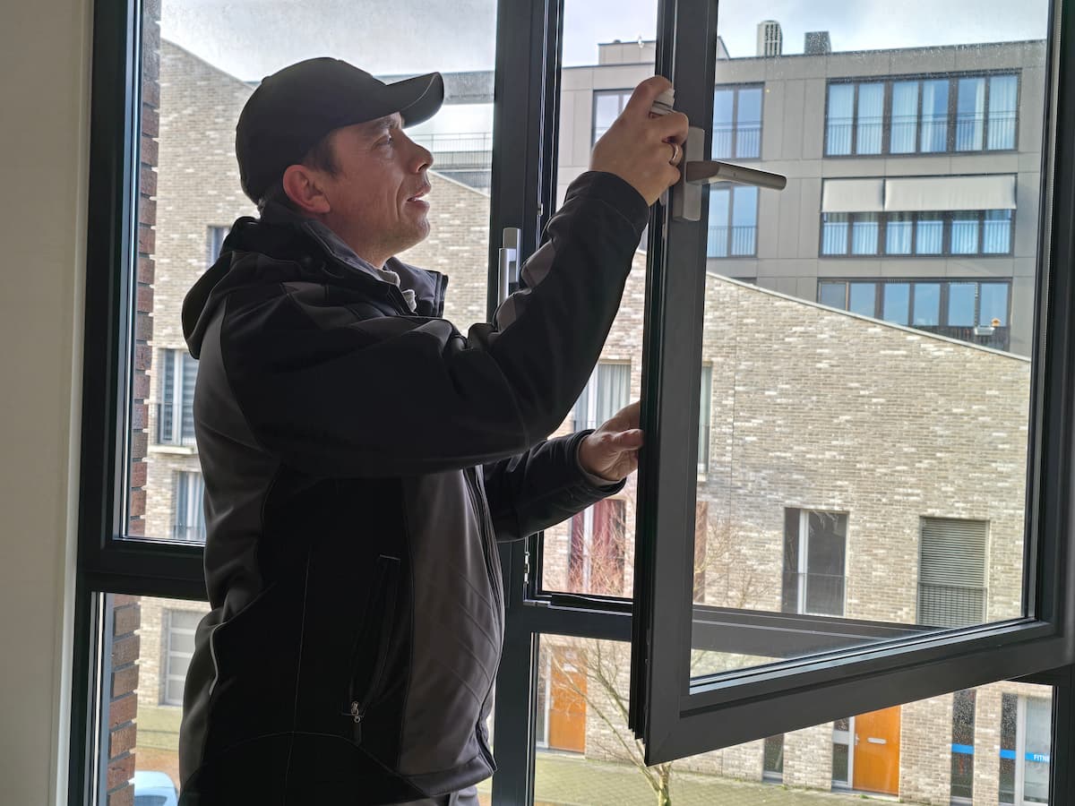 Slotenmaker inspecteert en repareert het sluitmechanisme van een modern kantelraam in een woning of kantoor.